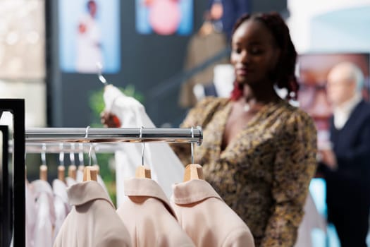 Selective focus of fashionable clothes in shopping centre, african american customer looking at shirt for formal wear. Stylish pregnant woman buying trendy merchandise and accessories