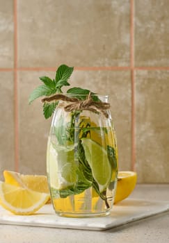 Lemonade in a transparent glass with lemon, lime, rosemary sprigs and mint leaves on a white background