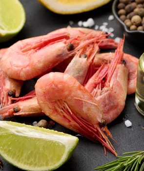 Boiled shrimp on a board, lemon slices, spices on a black background