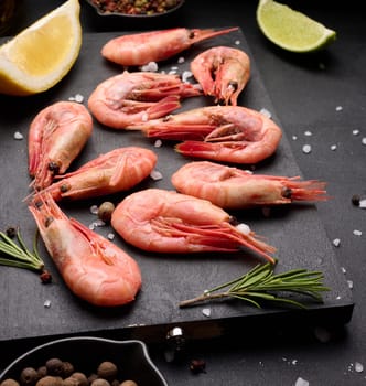 Boiled shrimp on a board, lemon slices, spices on a black background