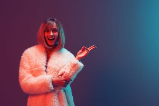 Cheerful adorable blonde woman in fluffy fur coat sparkly dress smile hold hand up posing isolated in blue turquoise red color light studio background. Neon party Fashion concept. Copy space Banner