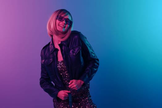 Smiling cheerful sexy beautiful blonde woman touch leather jacket sparkly dress trendy sunglasses posing isolated in blue pink color light studio background. Neon party Cyberpunk concept. Copy space