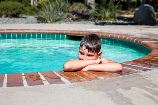 Concept of fun, health and vacation. Oudoor summer activity. A boy eight years old in swimming goggles is holding onto the side of the pool on a hot summer day.