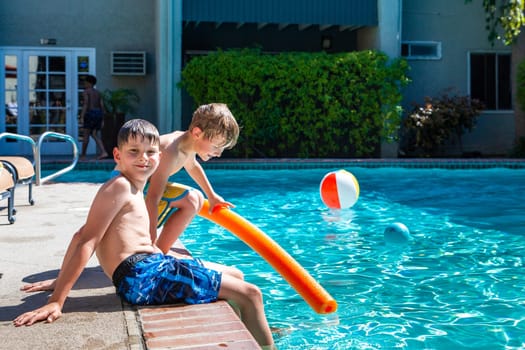 Concept of fun, health and vacation. Oudoor summer activity. Brothers boys eight and five years old with noodle sits near a pool in hot summer day.