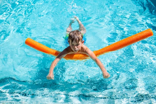 Concept of fun, health and vacation. Oudoor summer activity. A happy boy five years old is learning to swim with noodle in the pool on a hot summer day.