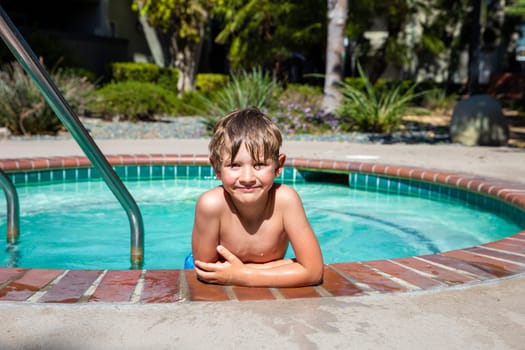Concept of fun, health and vacation. Oudoor summer activity. A happy boy five years old is holding onto the side of the pool on a hot summer day.
