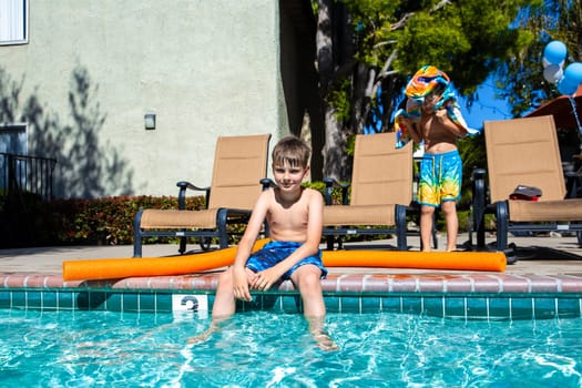 Concept of fun, health and vacation. Oudoor summer activity. Brothers boys eight and five years old with noodle sits near a pool in hot summer day.