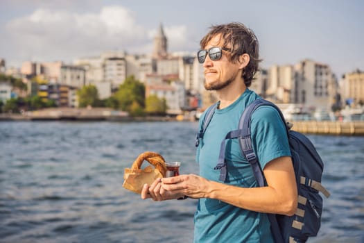 Man in Istanbul having breakfast with Simit and a glass of Turkish tea. Glass of Turkish tea and bagel Simit against golden horn bay and the Galata Tower in Istanbul, Turkey. Turkiye.