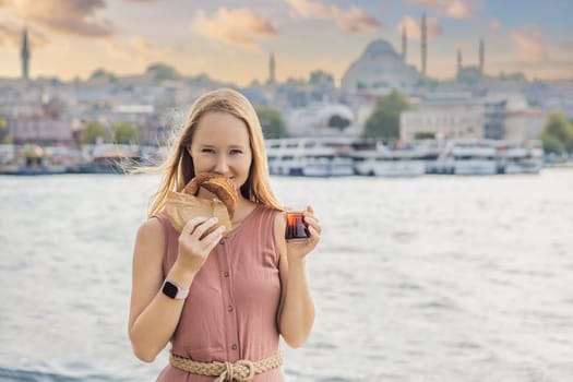 Woman in Istanbul having breakfast with Simit and a glass of Turkish tea. Glass of Turkish tea and bagel Simit against golden horn bay in Istanbul, Turkey. Turkiye.