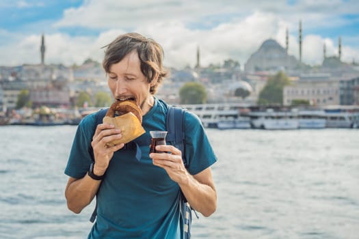 Man in Istanbul having breakfast with Simit and a glass of Turkish tea. Glass of Turkish tea and bagel Simit against golden horn bay in Istanbul, Turkey. Turkiye.