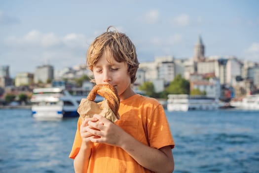 Boy in Istanbul having breakfast with Simit and a glass of Turkish tea. Glass of Turkish tea and bagel Simit against golden horn bay and the Galata Tower in Istanbul, Turkey. Turkiye. Traveling with kids concept.