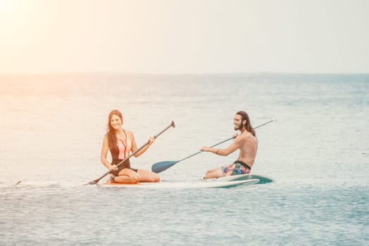 Sea woman and man on sup. Silhouette of happy young woman and man, surfing on SUP board, confident paddling through water surface. Idyllic sunset. Active lifestyle at sea or river
