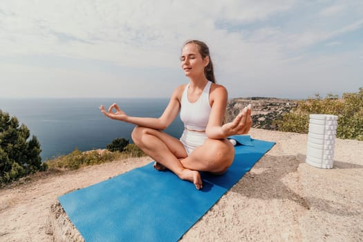 Middle aged well looking woman with black hair doing Pilates with the ring on the yoga mat near the sea on the pebble beach. Female fitness yoga concept. Healthy lifestyle, harmony and meditation.