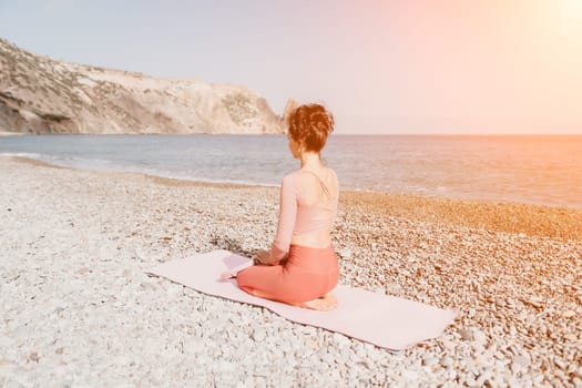 Middle aged well looking woman with black hair doing Pilates with the ring on the yoga mat near the sea on the pebble beach. Female fitness yoga concept. Healthy lifestyle, harmony and meditation.