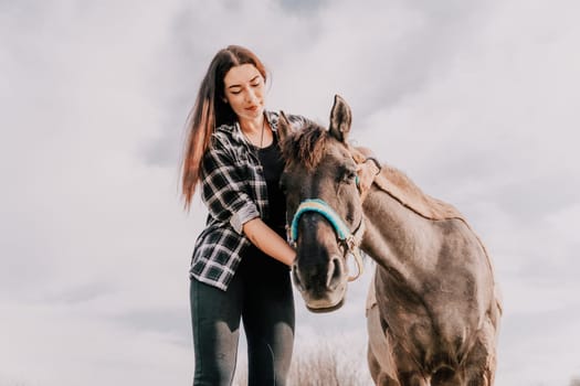 Cute happy young woman with horse. Rider female drives her horse in nature on evening sunset light background. Concept of outdoor riding, sports and recreation.