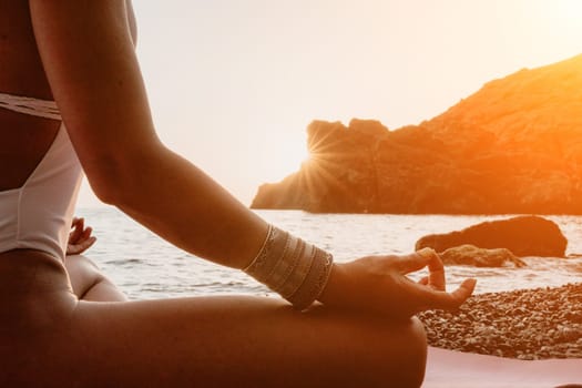 Young woman in swimsuit with long hair practicing stretching outdoors on yoga mat by the sea on a sunny day. Women's yoga fitness pilates routine. Healthy lifestyle, harmony and meditation concept.