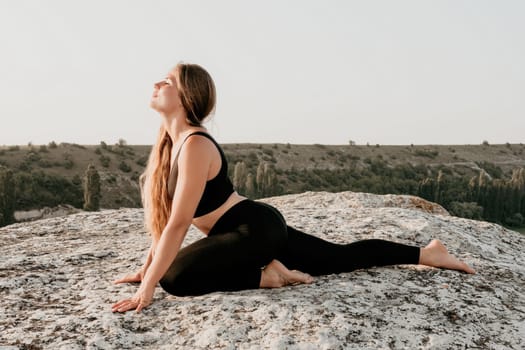 Well looking middle aged woman with long hair, fitness instructor in leggings and tops doing stretching and pilates on the rock near forest. Female fitness yoga routine concept. Healthy lifestyle.