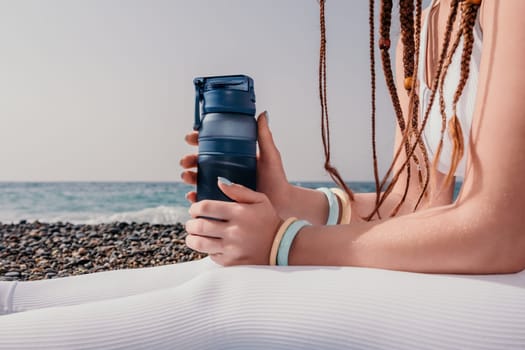 Woman yoga sea. Well looking middle aged woman with braids dreadlocks in white leggings and tops doing stretching pilates on yoga mat near sea. Female fitness yoga routine concept. Healthy lifestyle