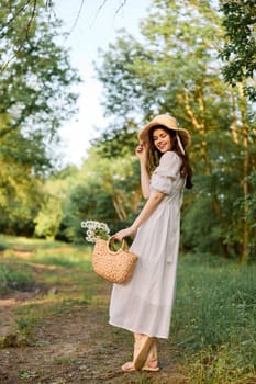 a woman in a light summer dress and a wicker hat stands in the forest with a basket of daisies in her hands. High quality photo
