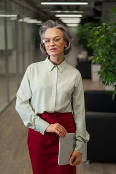 Attractive mature caucasian woman holding laptop while standing in office