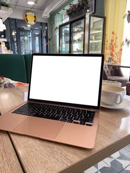 Mock up of generic laptop computer with blank copy space screen for your text or advertising content. Workspace of young freelancer: open notebook pc, cell phone and cappuccino on table in the cafe