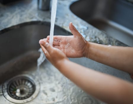 Child, hands and washing for clean hygiene, health and wellness with water in the kitchen. Hand of kid rinsing or cleaning with soap under running tap in basin to remove bacteria, virus or germs.
