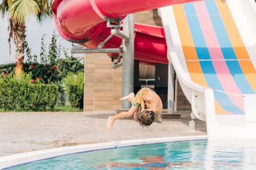 Child jumping and dives in swimming pool at sunny day. Kid boy refreshing and playing at heat weather, active vacation and healthy lifestyle. Happy summer.
