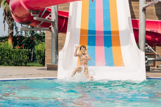 Child boy laughing while slide in pool after going down water slide at sunny day in water Aqua park. Kid refreshing at heat weather, active vacation and healthy lifestyle. Happy summer.