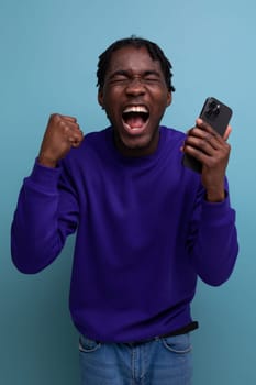 lucky winner african young man with dreadlocks with phone on studio background.