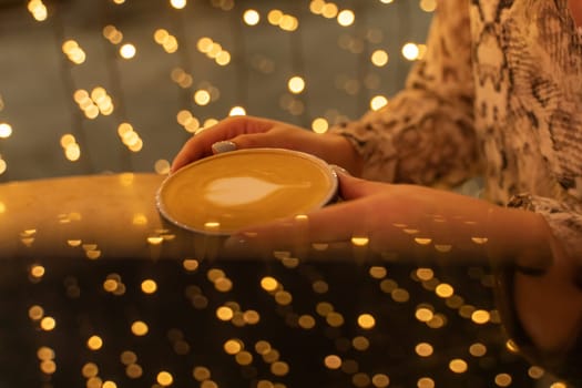 Close up Cup of coffee latte in coffee shop.Female hands holding a cup of coffee cup with heart shaped latte art foam on black wood table.