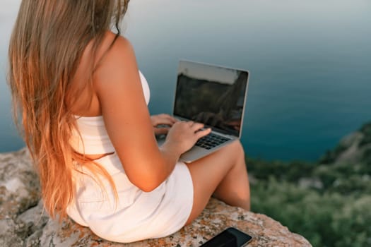 Freelance women sea working on the computer. Good looking middle aged woman typing on a laptop keyboard outdoors with a beautiful sea view. The concept of remote work