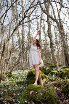 Snowdrops galanthus woman. She stands in a white dress on a meadow with snowdrops in a spring forest.