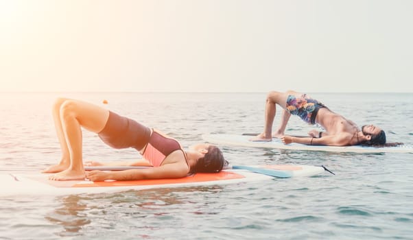 Woman man sup yoga. Happy young sporty couple practising yoga pilates on paddle sup surfboard. Female stretching doing workout on sea water. Modern family outdoor summer sport activity