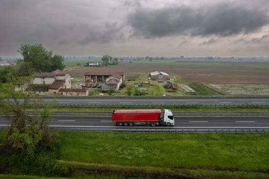 Cargo trucks and cars in the motorway a1 autostrada del sole aerial point of view in between padain plain rural fields