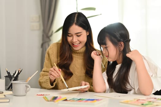 Cheerful little asian girl drawing with her mother in living room. Family home leisure concept.