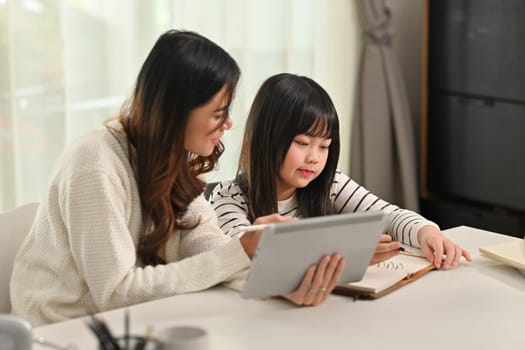 Interested Asian girl doing home working with tutor at home. Homeschooling and learning concept.