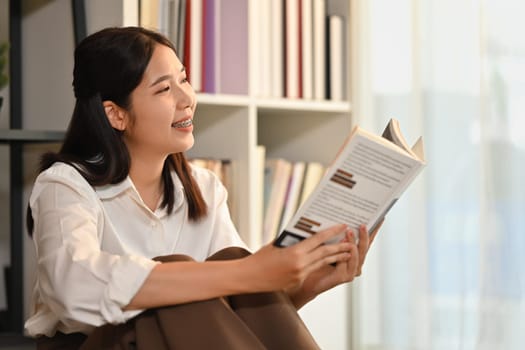 Beautiful woman sitting floor in living room and reading a book, spending leisure weekend time at home.