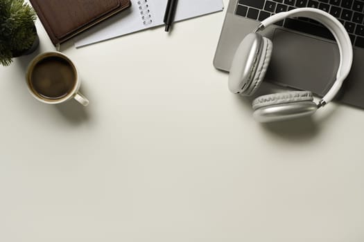 Top view of laptop, headphone, empty notepad and coffee cup on white table. Copy space for your text.