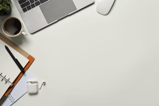 Top view of laptop computer, notepad, cup of coffee and earphone on white working desk.