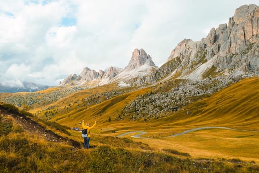 A hiker with outstretched arms, relishing the joy of exploration amidst the towering mountains of the renowned Giau Pass.