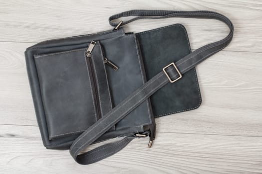 Leather shoulder bag for men with belt on gray wooden background. Men's accessories. Top view.