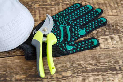 Garden black glove, pruner and hat on wooden board. Garden tools and equipment.