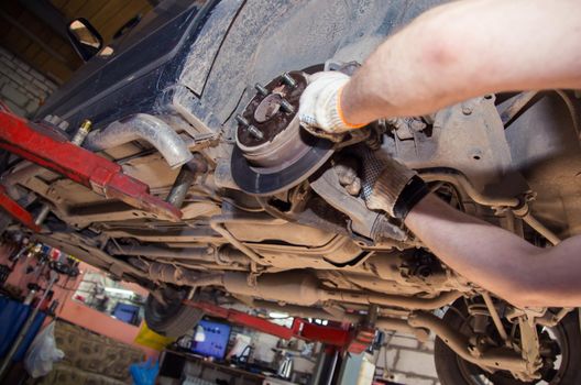 Gloved hands install the rear wheel hub support. In the garage, a person changes the failed parts on the vehicle. Small business concept, car repair and maintenance service.