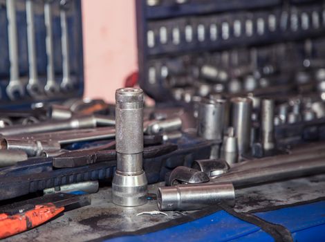 A set of sockets for a wrench, defocused on a metal workbench in a workshop. In the garage are tools for repairing broken vehicle parts. Small business concept, car repair and maintenance service.