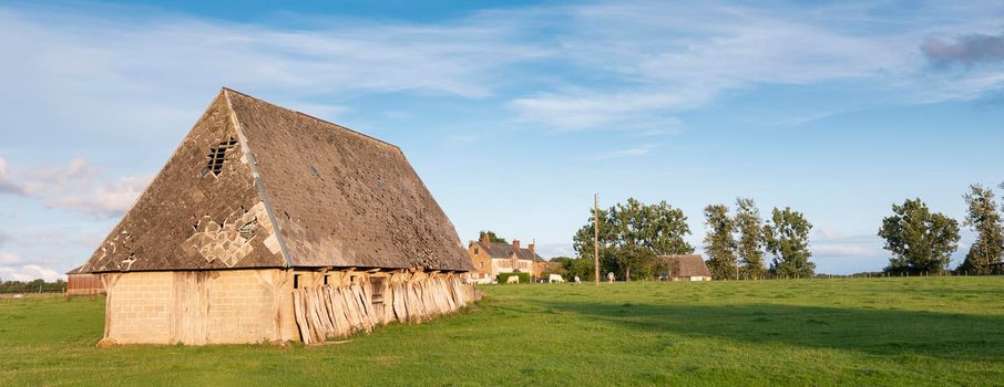 old barn and sheds under blue sky in warm evening light in regional park boucles de la seine near rouen in france