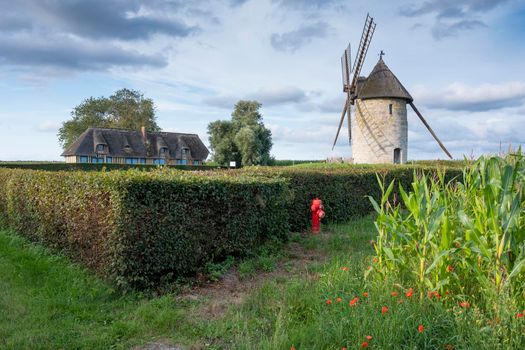 beautiful old windmill and traditional farm in french normandy under blue summer sky