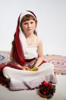 Portrait of Little girl in a stylized Tatar national costume with berries and a brush of grapes on a white background in the studio. Photo shoot of funny young teenager who is not a professional model