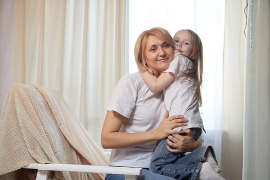 Happy loving family with mother and daughter having hugs in living room. Woman mom and small child girl inside of home