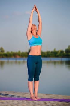 girl doing yoga exercises on the river bank at sunset