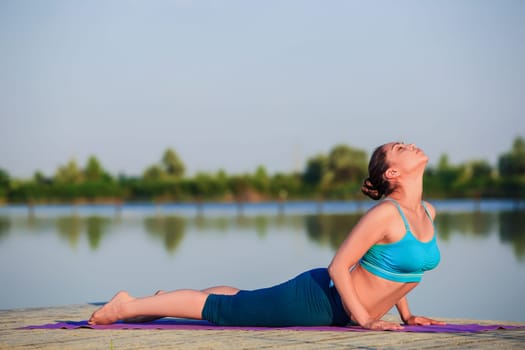 girl doing yoga exercises on the river bank at sunset